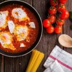 black frying pan with spaghetti sauce near brown wooden ladle and ripe tomatoes